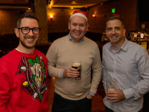 Three men hold beers wearing Christmas hats